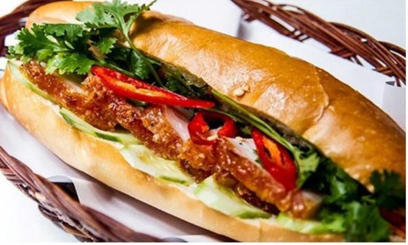 Thịt heo quay kẹp bánh mì, ăn kèm với đồ chua và rau thơm.